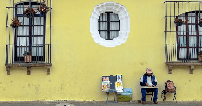 A man sketches in front of a bright yellow wall in Antigua, Guatemala