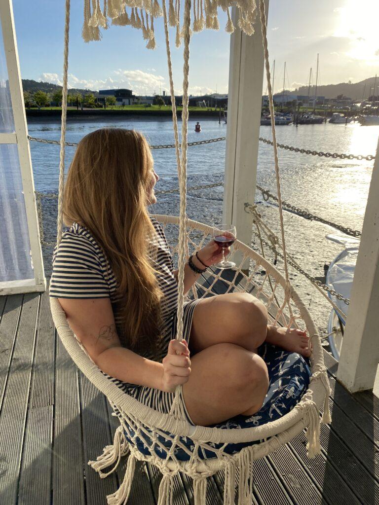 Girl sitting in a hanging chair with a glass of wine watching the sunset