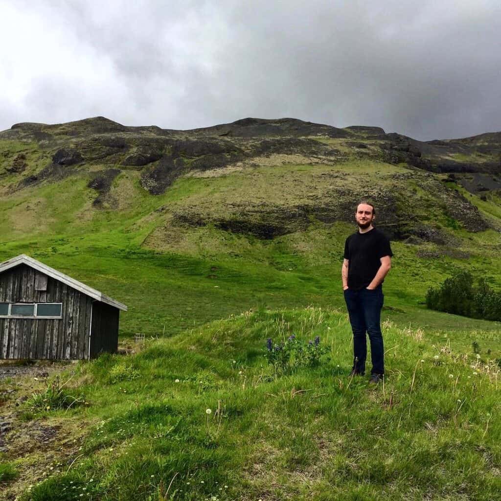 Man standing in a green field with an old wooden house