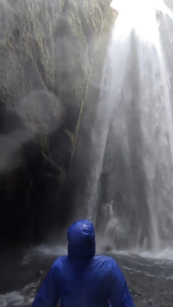 Girl in rain jacket looking at waterfall in cave