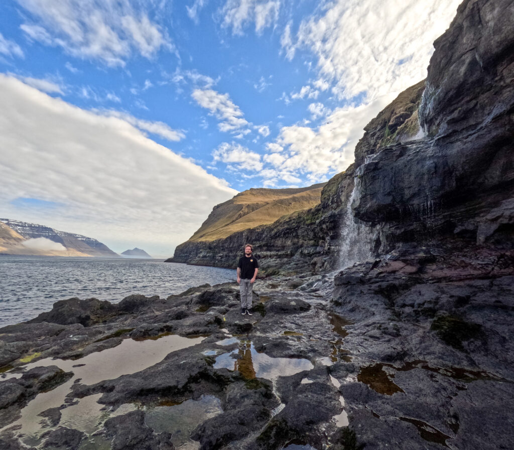 Man standing in Kalsoy, Faroe Islands next to a waterfall