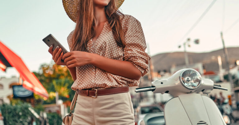 Woman texting next to vespa on vacation
