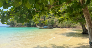 Loh Moo Dee Beach with clear turquoise water, golden sand, and a small boat anchored near shady green trees