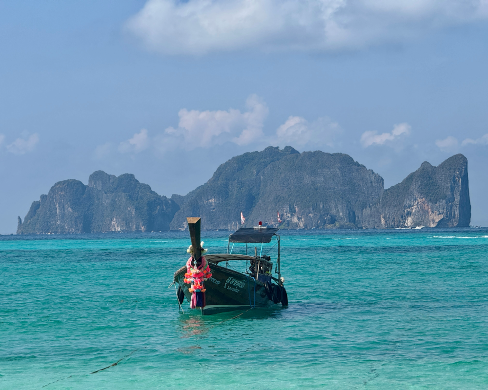 Traditional long-tail boat anchored in turquoise water with limestone karst islets in the distance under a blue sky
